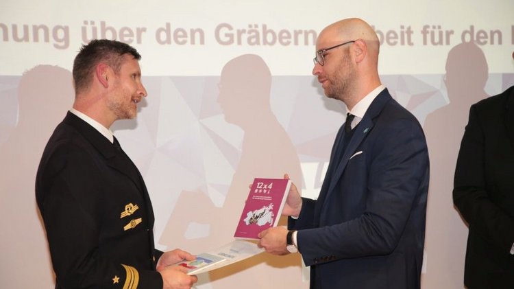 Herr Schinschke, Landesgeschäftsführer Volksbund übernimmt die Ehrung eines Soldaten der Marinetechnikschule aus Stralsund für die Beteiligung an einem Arbeitseinsatz auf einer Kriegsgräberanlage in Lettland mit einer Urkunde, der Ehrenfliese des Volksbundes und dem Reiseführer des Heimatverbandes M-V
